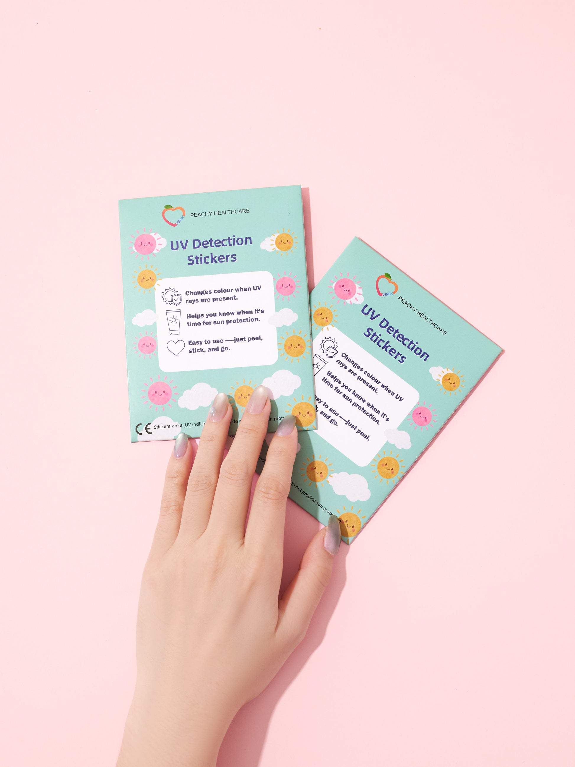Hand holding UV Detection Stickers cards showing the how-to-use instructions, on a pink background